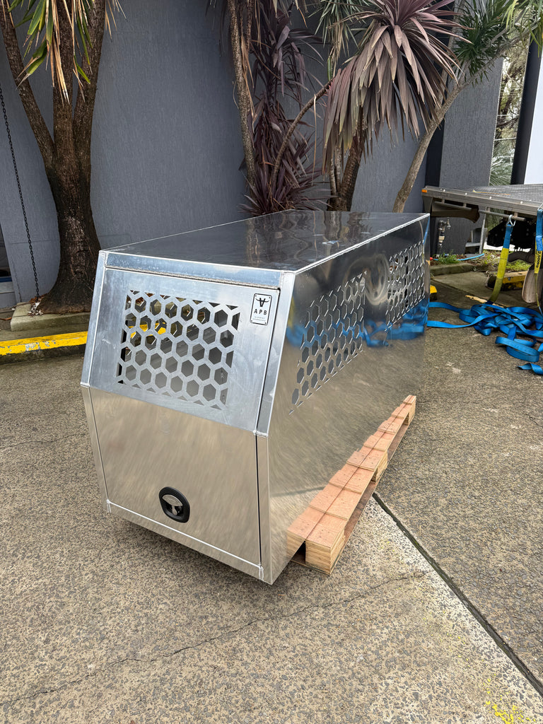Apboxes metal dog box shown at an angle, displaying its side in a workshop setting.